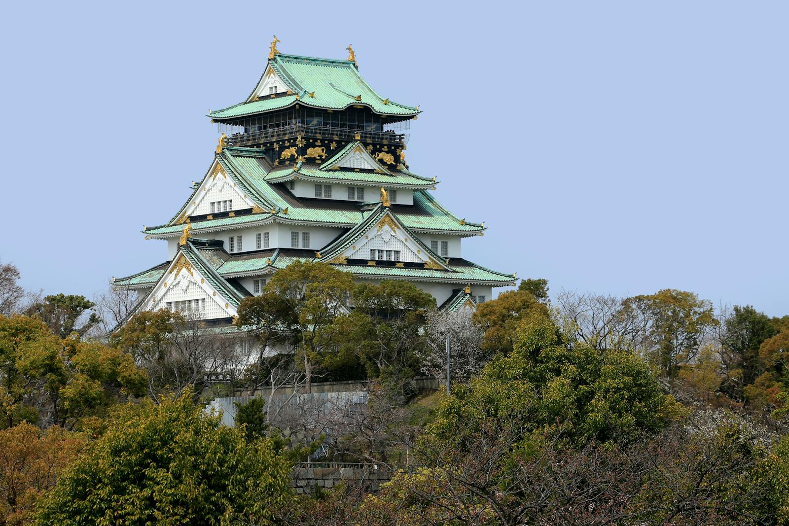 A stunning view of Osaka Castle surrounded by lush greenery under clear blue skies.